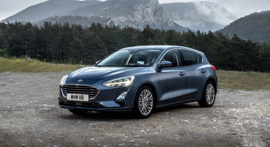 En blå Ford parkerad på en grusplan bland bergen