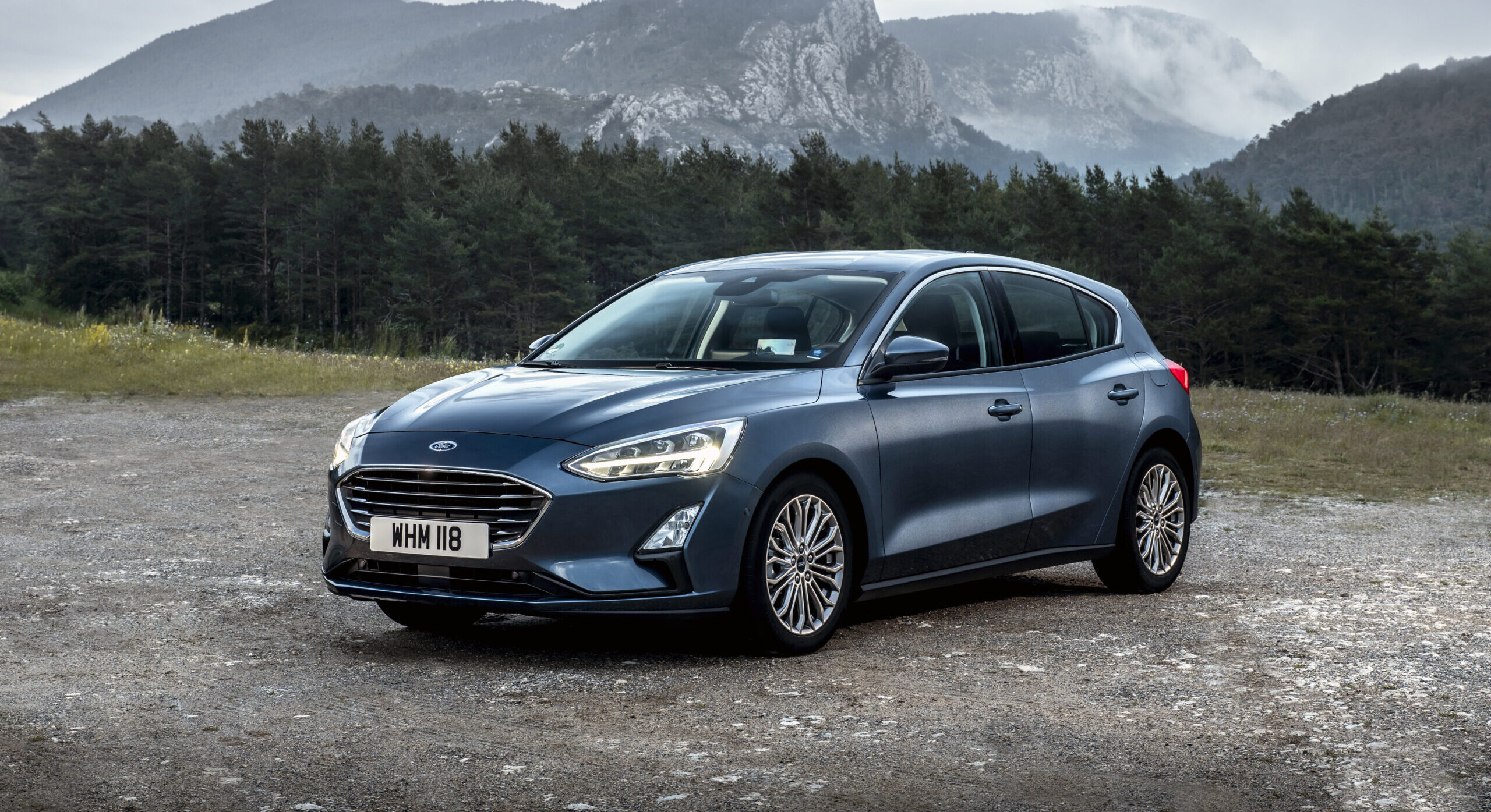 En blå Ford parkerad på en grusplan bland bergen